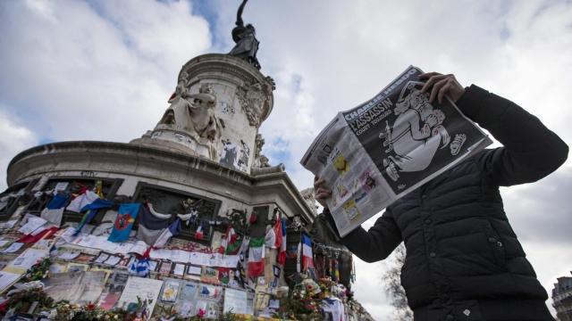 Un hombre pasa leyendo 'Charlie Hebdo' ante el homenaje por el aniversario de la tragedia.