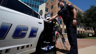 An officer touches a police car during a personal moment of silence at a makeshift memorial at Police Headquarters following the multiple police shooting in Dallas