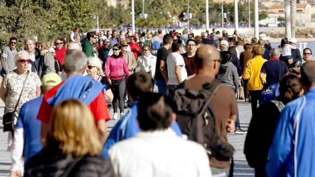Numerosos turistas pasean junto a una playa disfrutando del sol