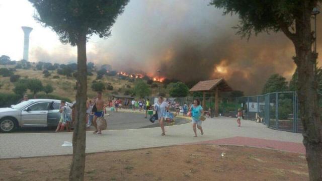 Las personas huyen del lugar con las llamas al fondo