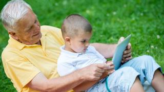 Un abuelo y su nieto manejan juntos una tablet.