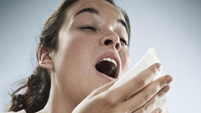Una mujer estornudando muy fuerte.