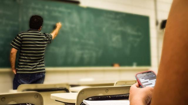 Imagen de archivo de un alumno usando un móvil en un aula