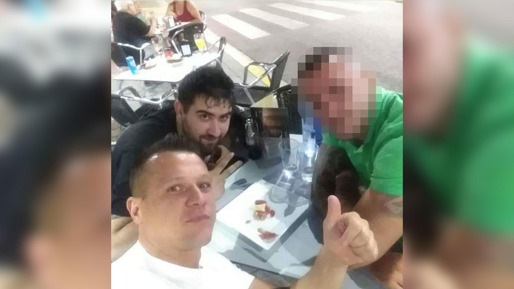 La víctima, de blanco y levantando el pulgar, junto a su asesino, de negro.