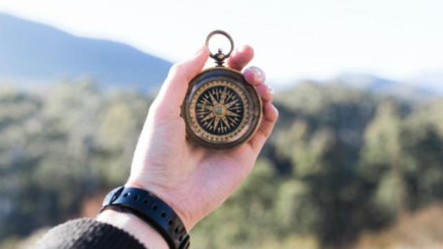 Una persona sostiene una brújula ante un paisaje agreste.