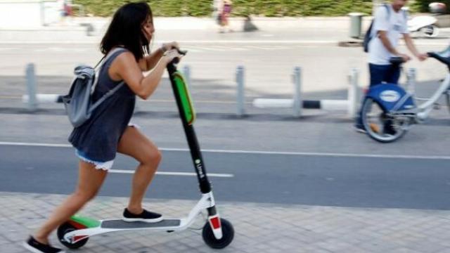 Joven circulando con patinete por la acera