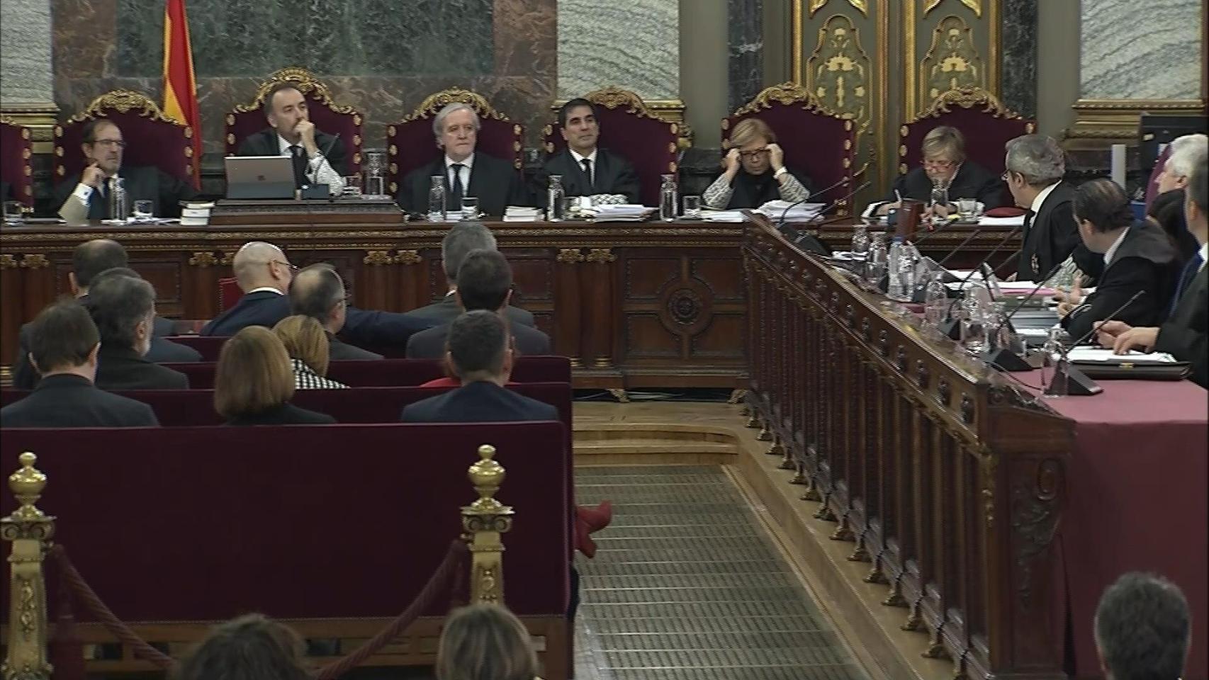 Imagen tomada de la señal institucional del Tribunal Supremo de los jueces (al fondo), los procesados (a la izqda. de espaldas) y la acusación (dcha.).