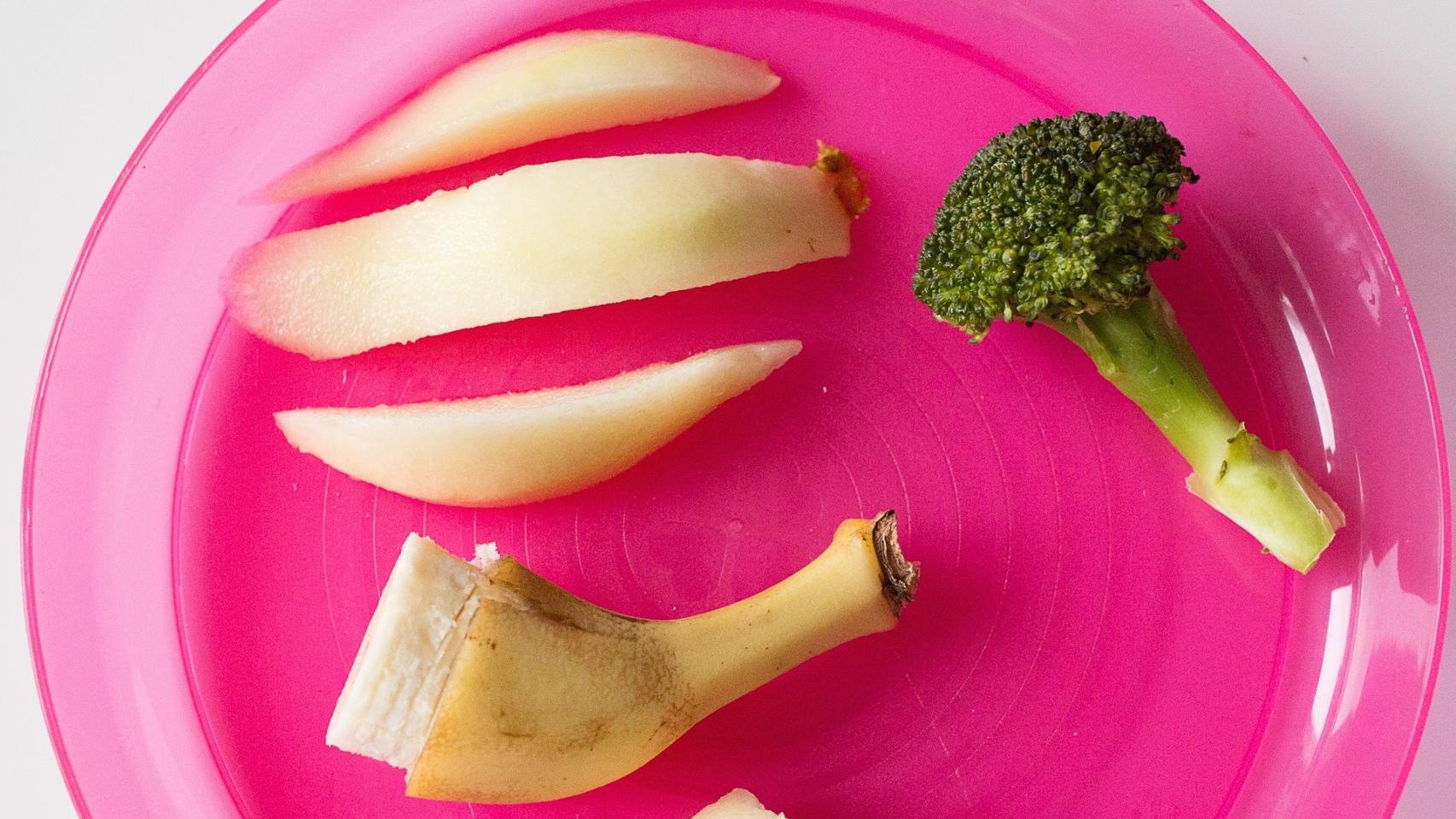 Un plato con unos trozos de manzana, brócoli y un plátano.
