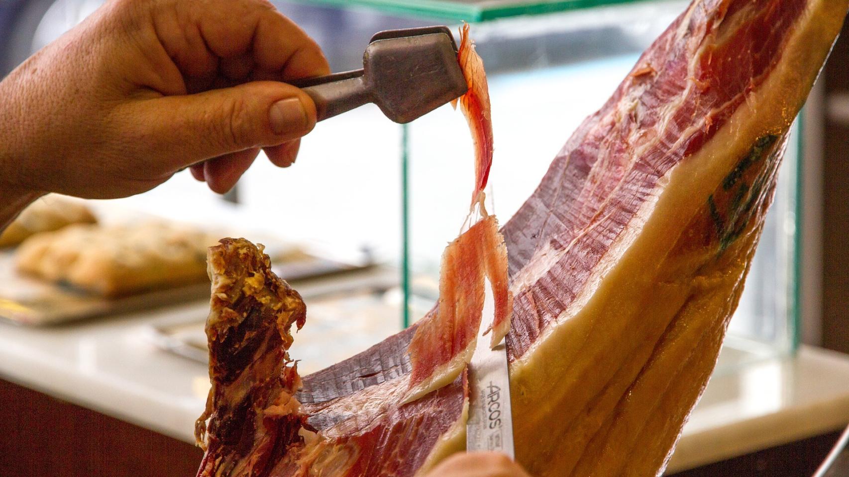 Un hombre cortando un trozo de jamón con un cuchillo.