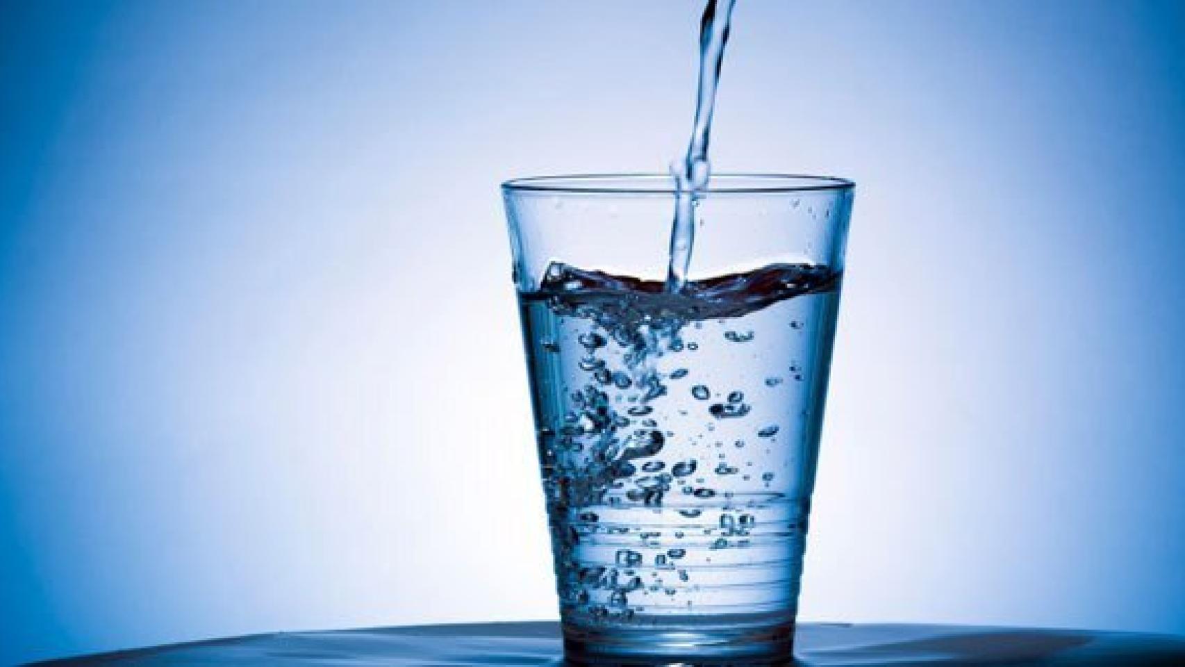 Un vaso de agua sobre el que cae un chorrito del líquido elemento.