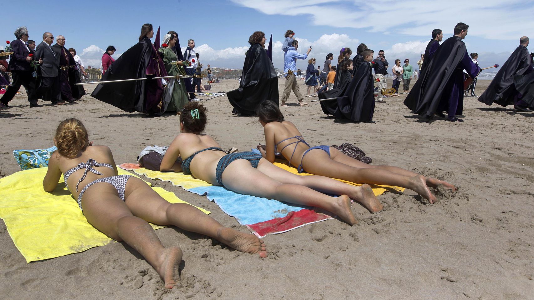 Penitentes del Santísimo Cristo del Salvador y el Amparo pasan frente a bañistas en Valencia en la Semana Santa de 2011.