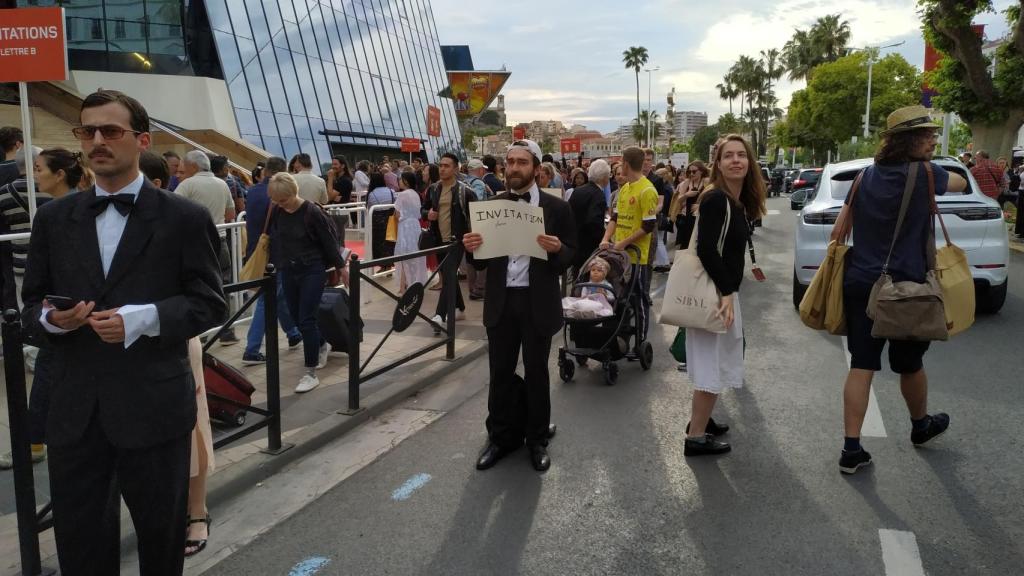 Un chaval al lado del Palais con su traje y su cartelito pidiendo una entrada.