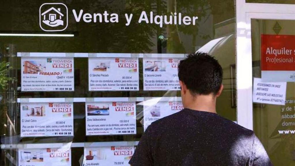 Una persona mirando el cartel de una agencia inmobiliaria en una imagen de archivo.