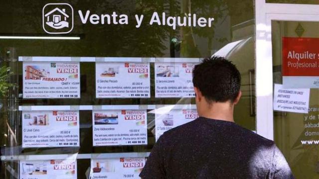Una persona mirando el cartel de una agencia inmobiliaria en una imagen de archivo.