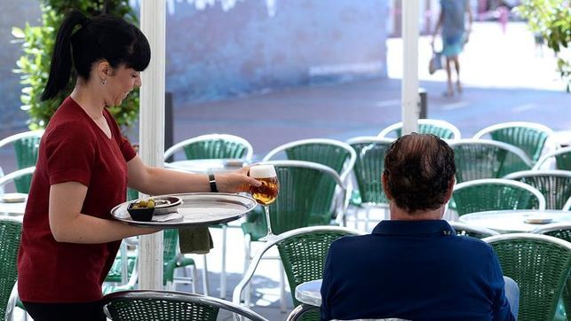 Una camarera atiende a un cliente en una terraza.