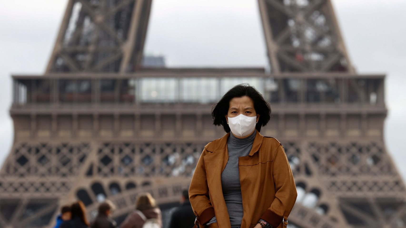 Una mujer camina con mascarilla junto a la Torre Eiffel, en París.