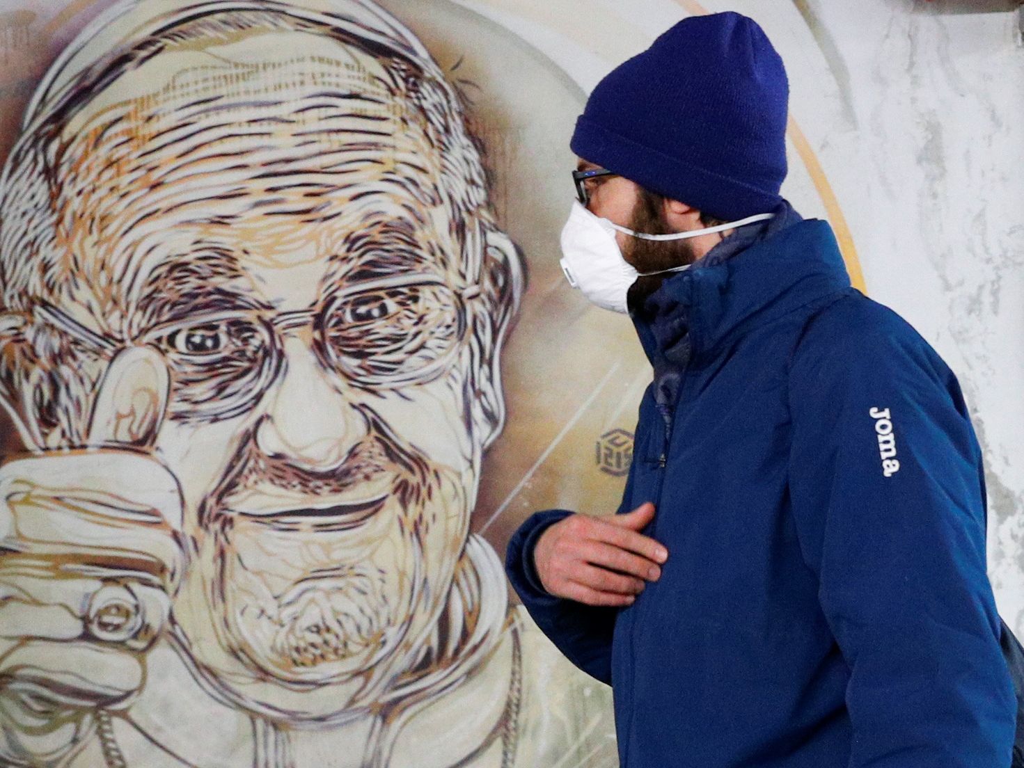 Un hombre con una mascarilla pasa por delante de un mural de Papa, en Roma.