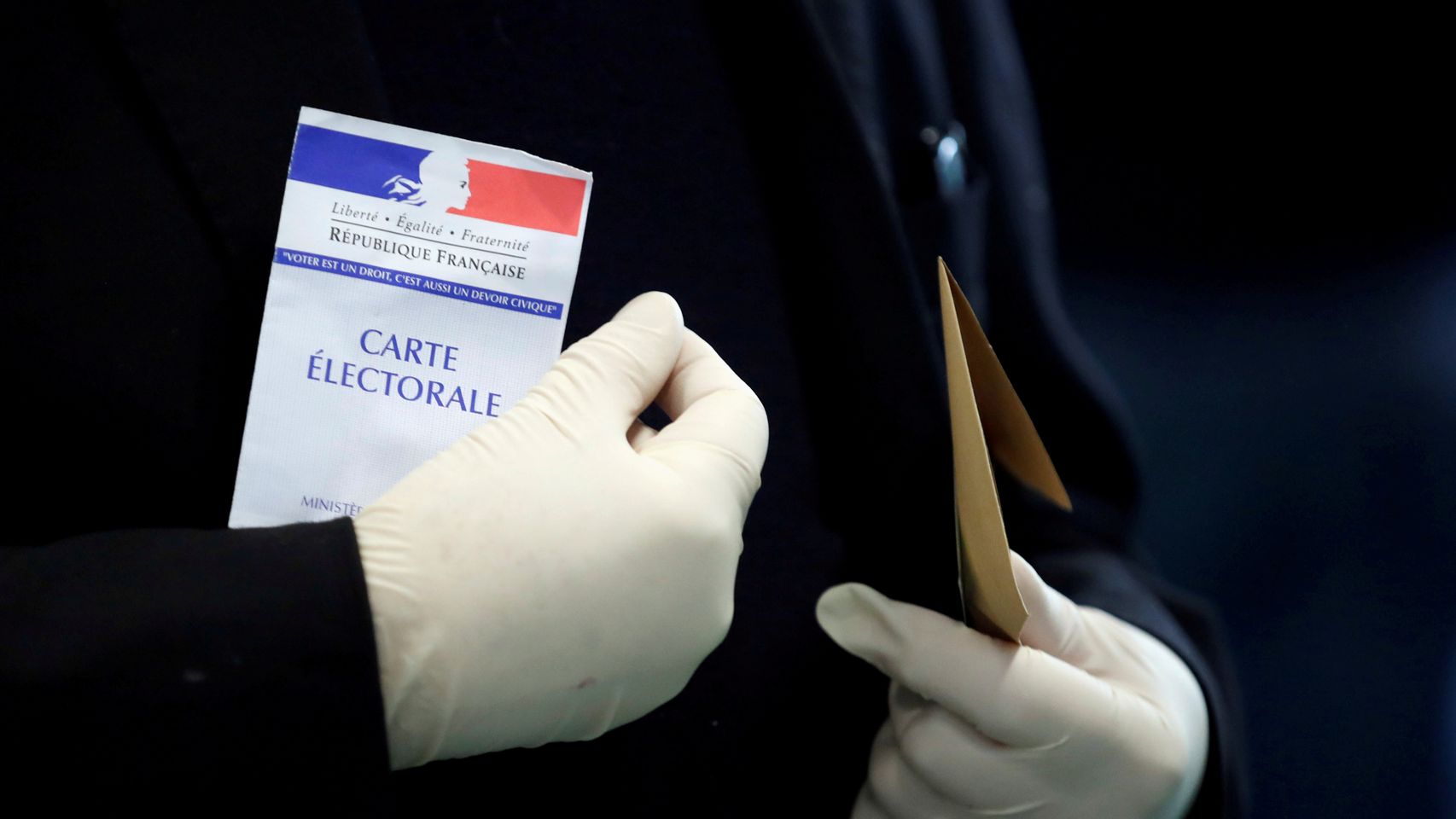 Un hombre con guantes de látex porta su tarjeta electoral antes de votar, en París.