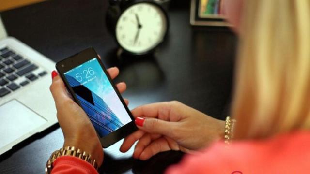 Una mujer usando su teléfono móvil delante de un ordenador.