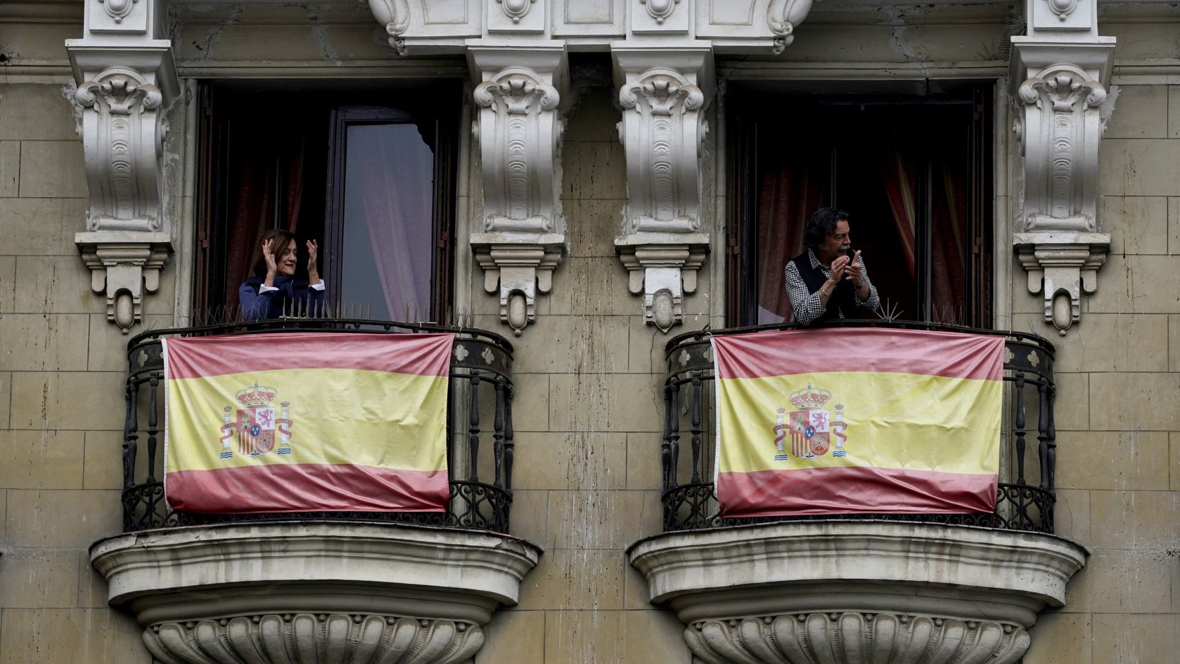 Dos ciudadanos aplauden desde los balcones de sus casas, en Madrid.