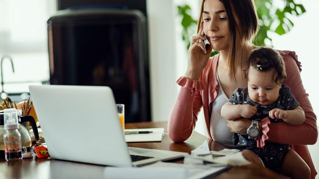 Una mujer teletrabajando mientras cuida a su hijo.