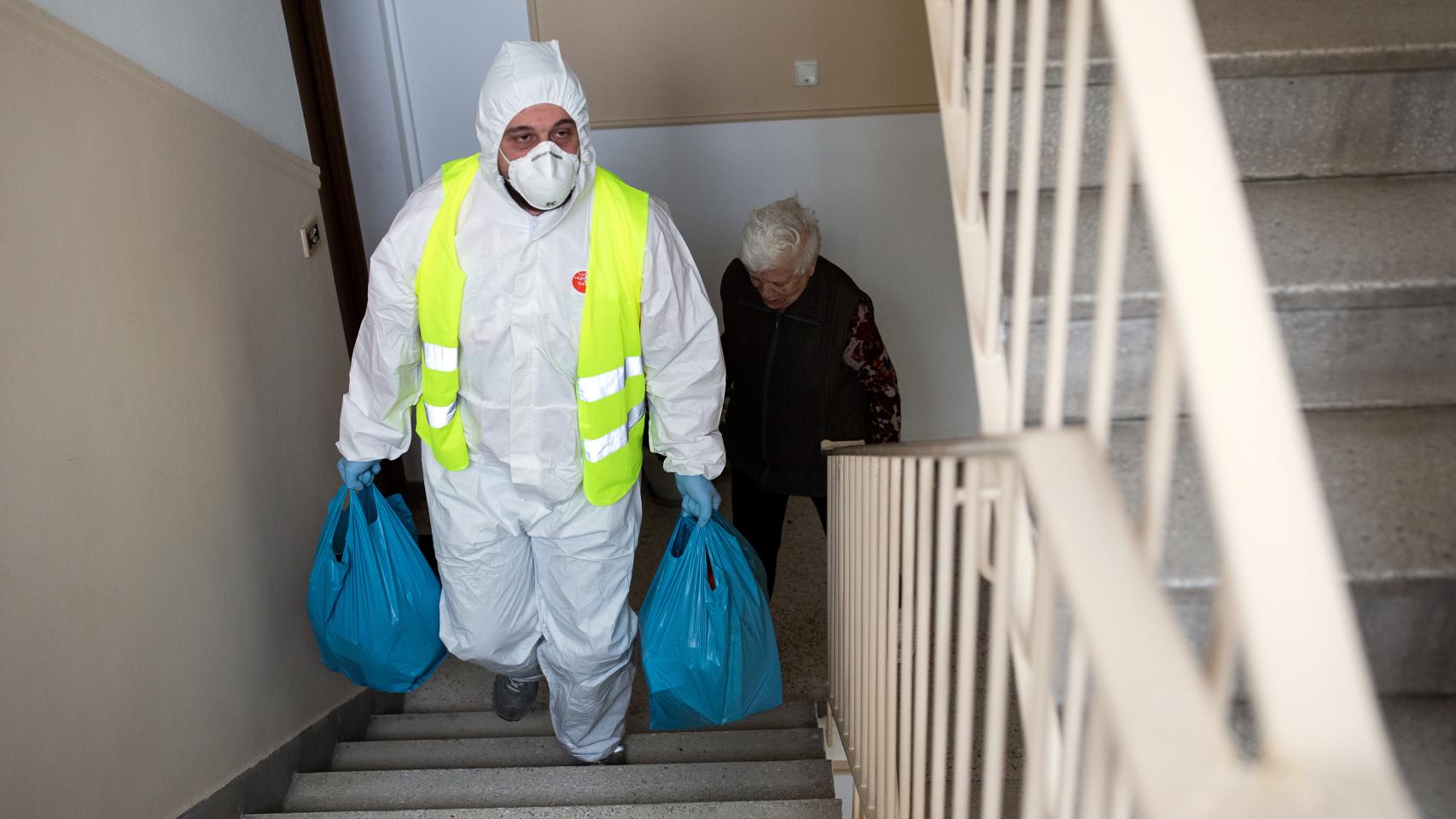 Un voluntario ayuda a una anciana a subir las bolsas de la compra, en Atenas.