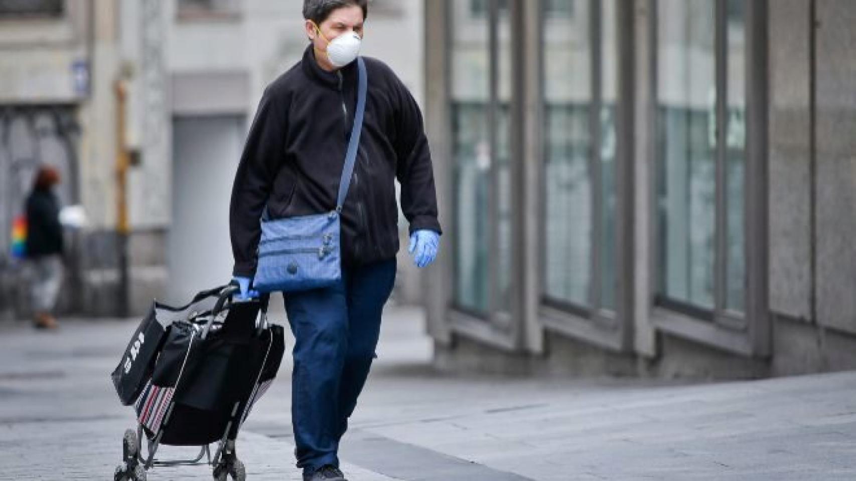 Una mujer con mascarilla, guantes y un carro de la compra.