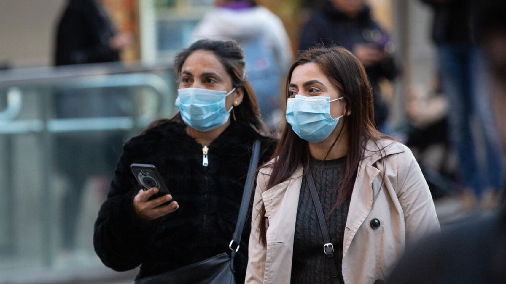 Dos mujeres andan por la calle con mascarillas en la cara.