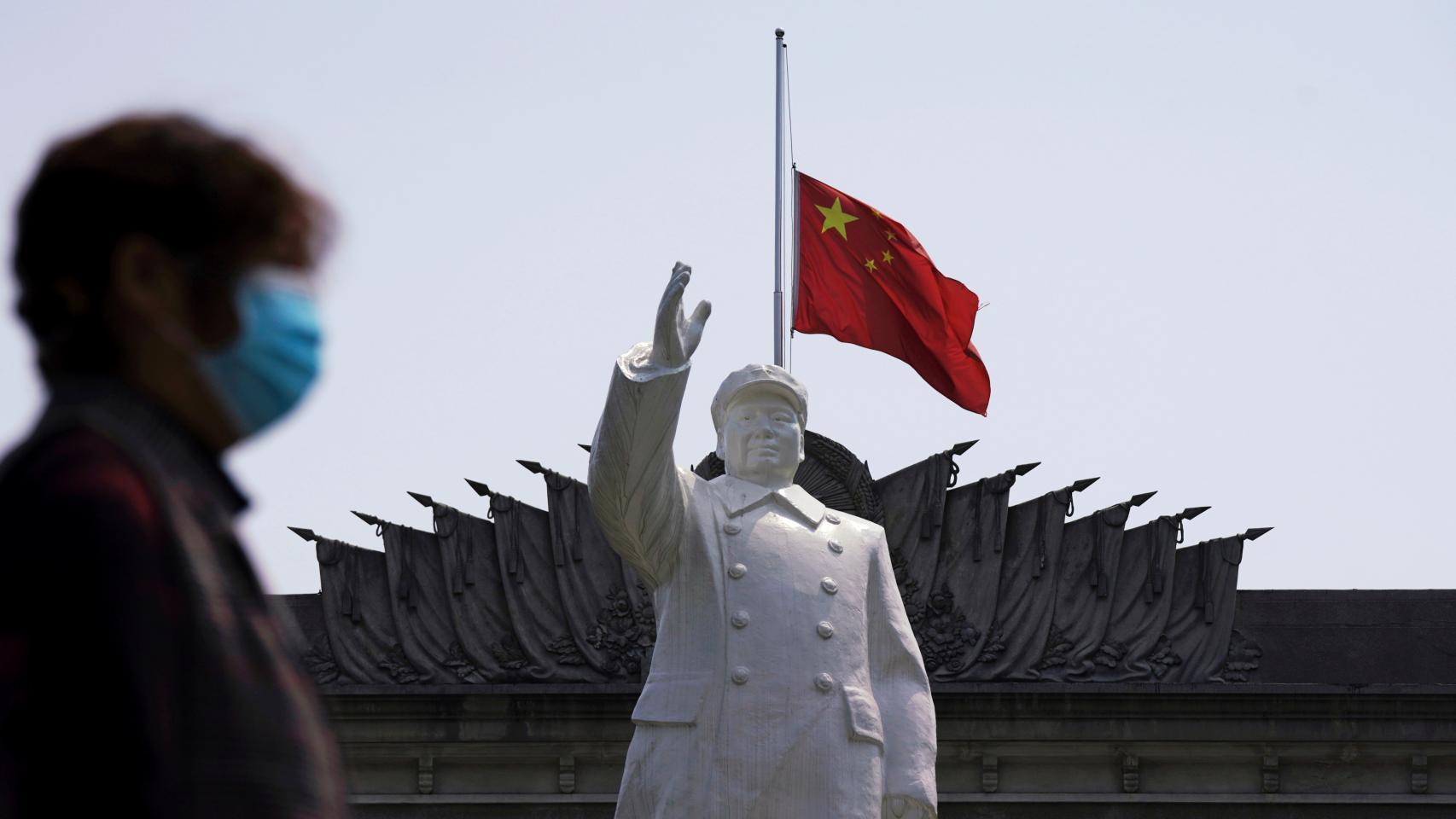 Una mujer con mascarilla pasa delante de una estatua de Mao Zedong en Wuhan.
