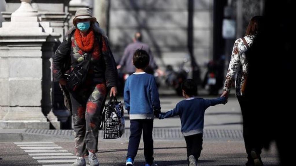 Niños y adultos con mascarillas andando por la calle.