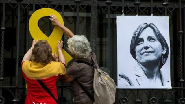 Dos mujeres colocan un lazo amarillo junto a un retrato de Carme Forcadell./