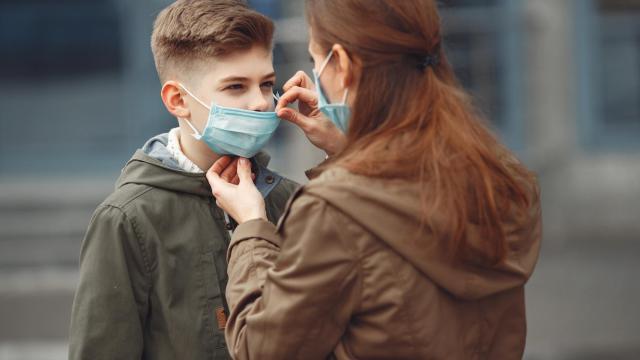 Una madre le ajusta la mascarilla quirúrgica a su hijo.