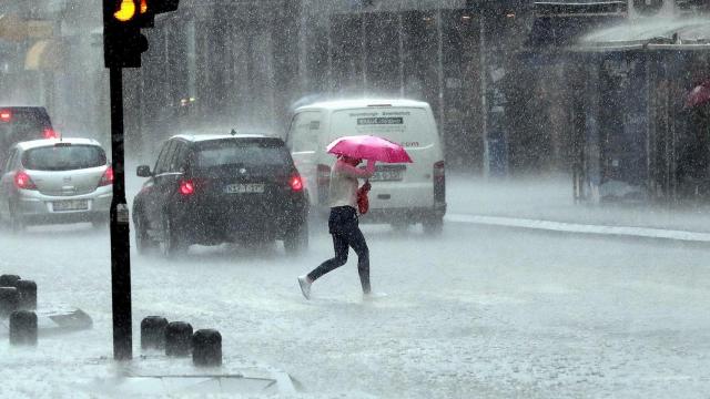 Una mujer cruza la calle bajo una lluvia torrencial.