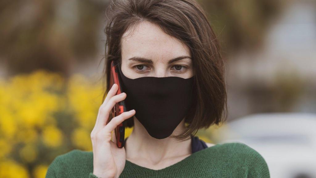 Mujer con mascarilla usa un móvil.