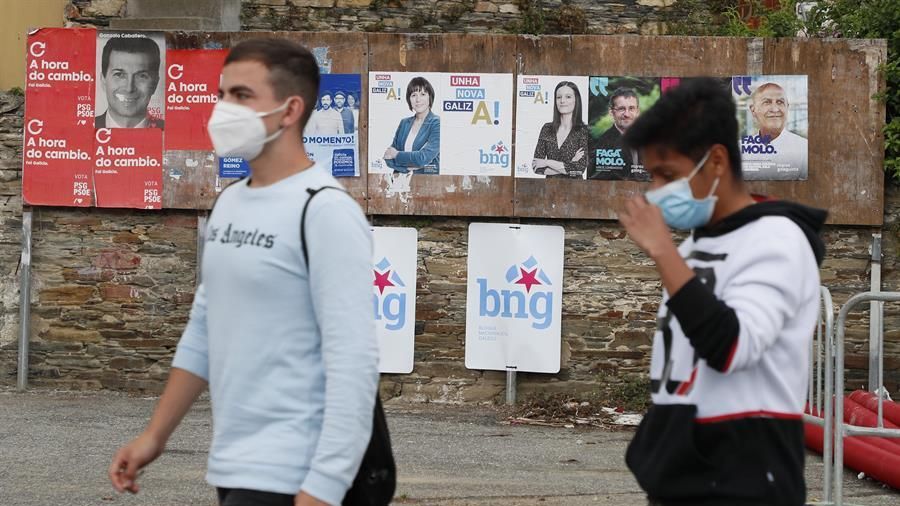 Dos jóvenes con mascarillas pasan por delante de varios carteles electorales, este viernes en Foz (Lugo).