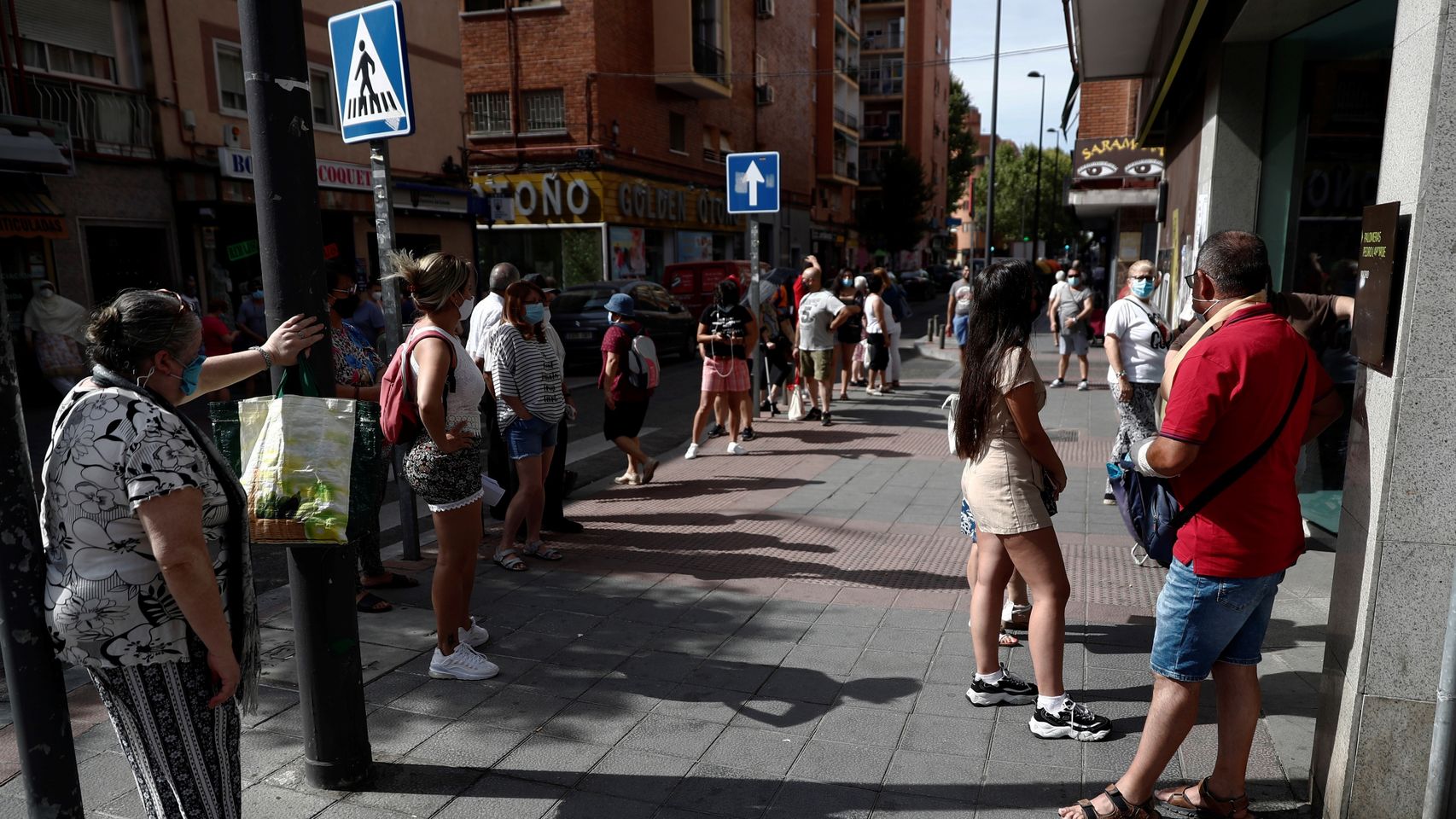 Unas personas pasan calor haciendo cola para entrar al banco en Madrid.