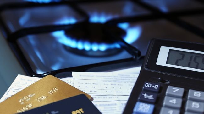 Montaje con la imagen de una cocina que funciona con gas natural, junto a una calculadora, dos tarjetas de crédito y varios papeles.
