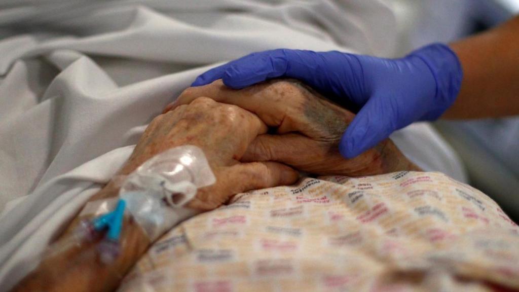 Un sanitario coge las manos de una persona anciana.