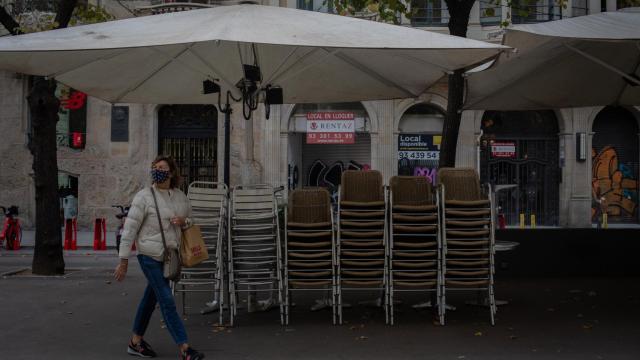 Una mujer pasa junto a la terraza recogida de un bar.