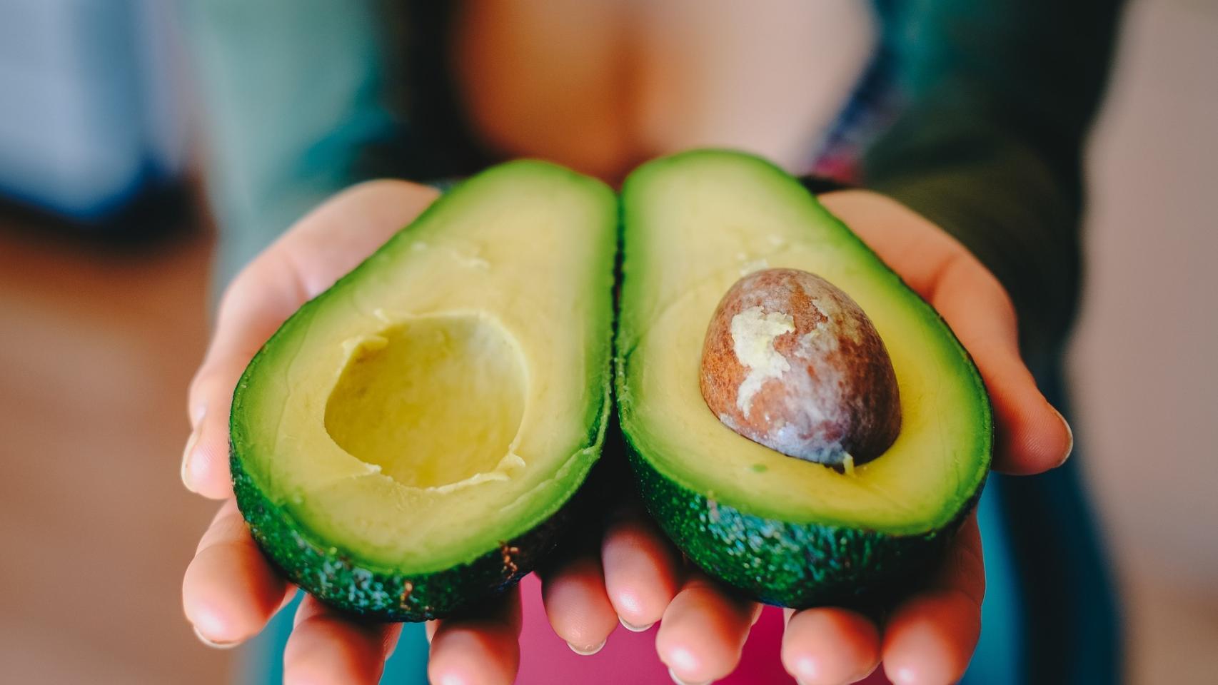 Una joven sostiene un aguacate partido por la mitad.