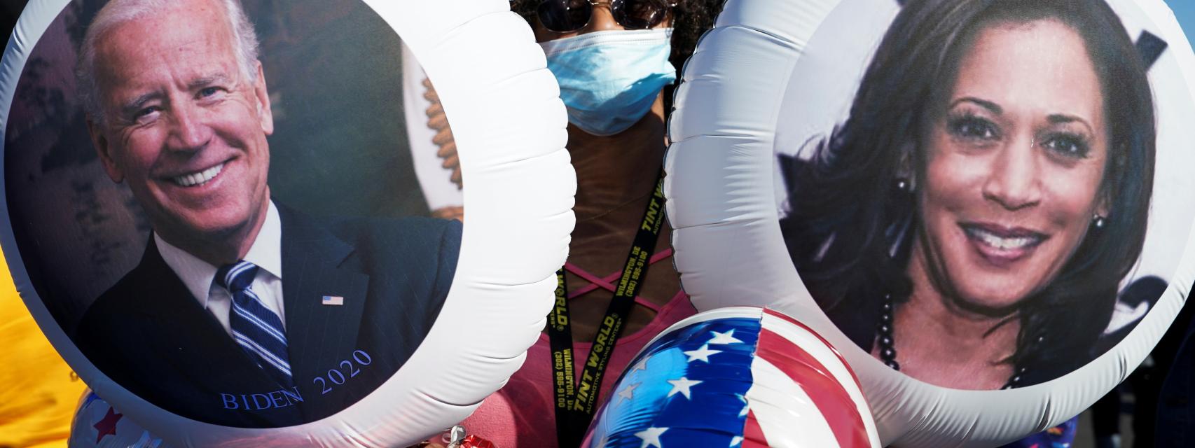 Una mujer celebrando la victoria con dos globos de Biden y Harris.