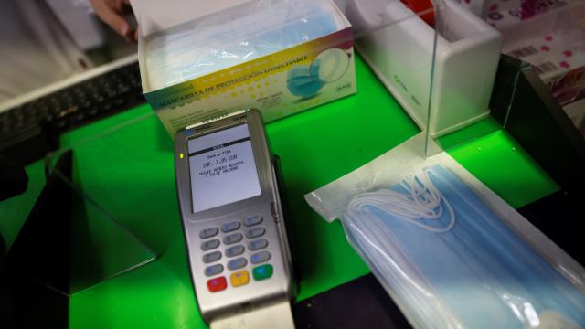 Una persona, pagando con datafono, por un paquete de mascarillas quirúrgicas.
