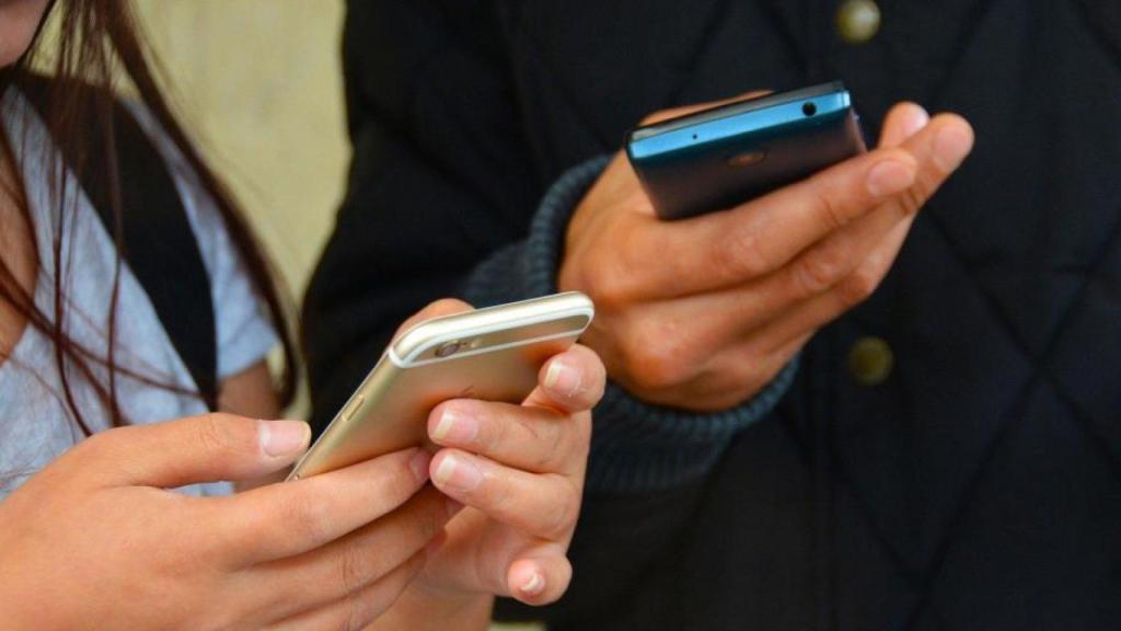 Dos personas con el teléfono móvil en sus manos.
