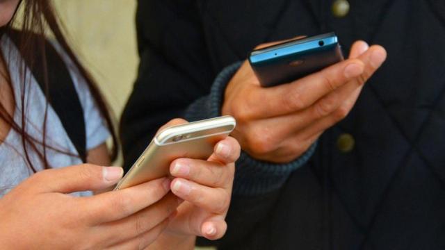 Dos personas con el teléfono móvil en sus manos.