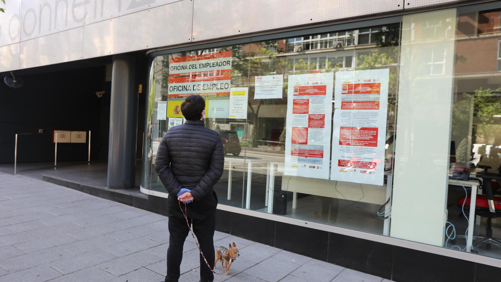 Un hombre pasa con su perro frente a una oficina de Empleo en Madrid.