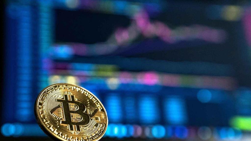 Una moneda de bitcoin sobre unas gráficas de cotización.