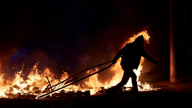 Un alborotador lanza una valla ante una barricada de fuego en la calle Aragó de Barcelona, en las protestas violentas por el encarcelamiento de Pablo Hasél.