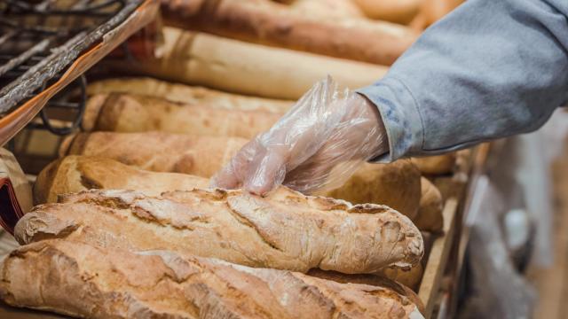 Una persona toma una barra de pan con un guante.