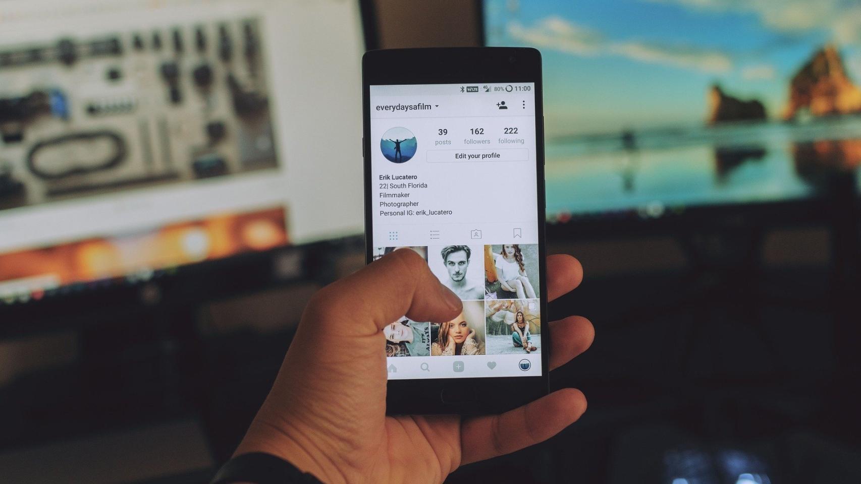 Un teléfono móvil consulta una red social con varias ordenadores al fondo.