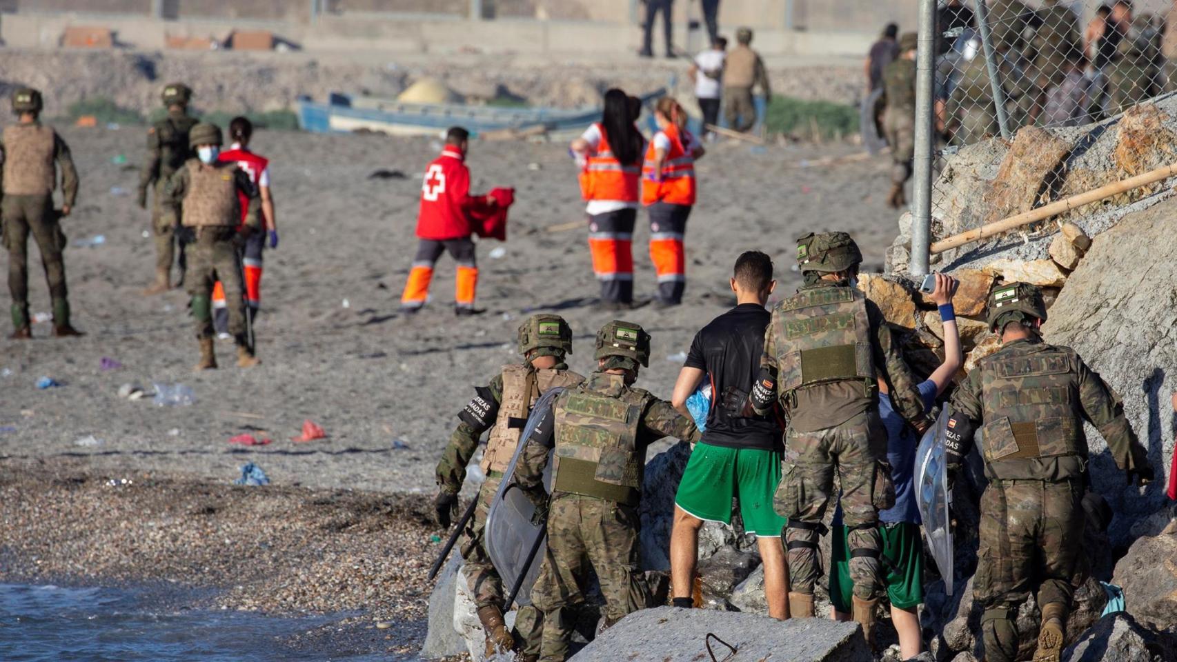 Miembros del Ejército ayudan a varios inmigrantes a su llegada a la playa de El Tarajal. Efe